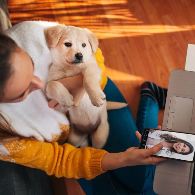 A woman holding a puppy while video chatting with a vet on her phone