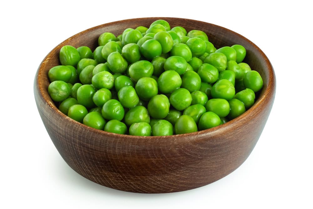 Fresh green garden peas in a dark wood bowl